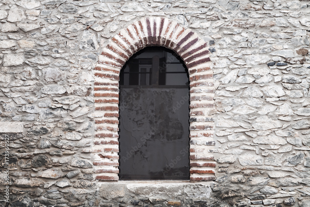 Arched window in old gray stone wall