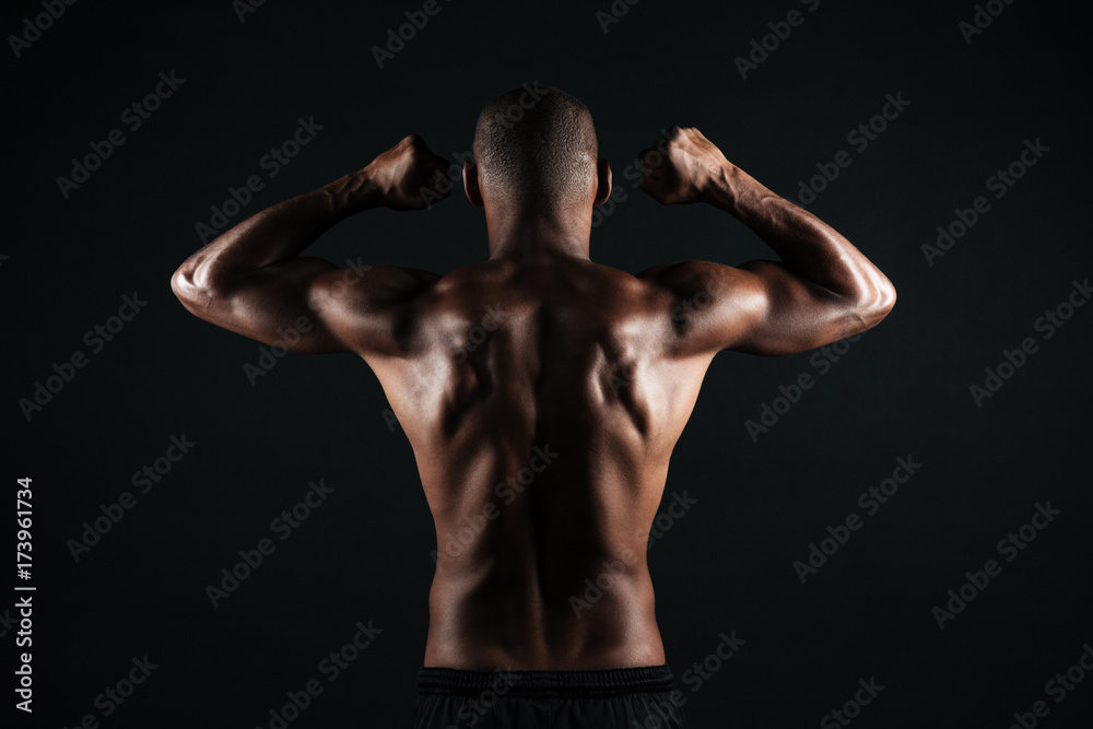 Portrait of young afro american sports man, standing back, showing musculs