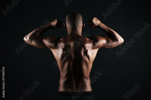 Portrait of young afro american sports man, standing back, showing musculs photo