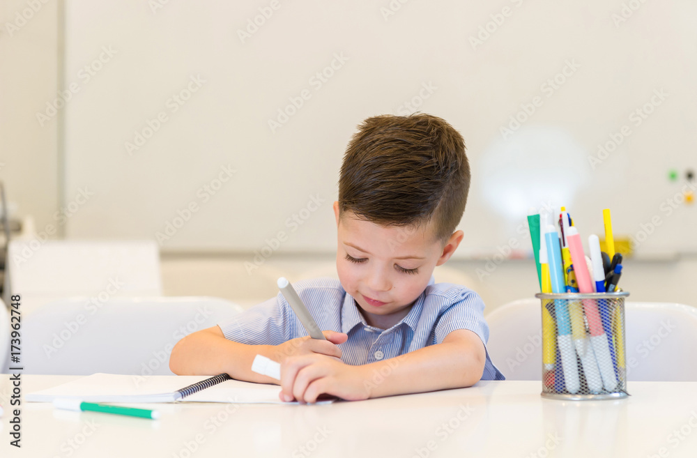 child preschooler boy drawing on booklet ,while sitting on the desk in the classroom child preschooler boy drawing on booklet ,while sitting on the desk in the classroom