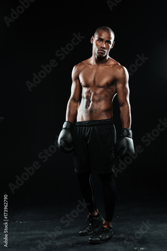 Young afroamerican boxer in gloves  standing on black background