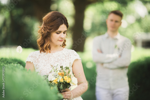 Bride posing and smiles while groom waits on the background