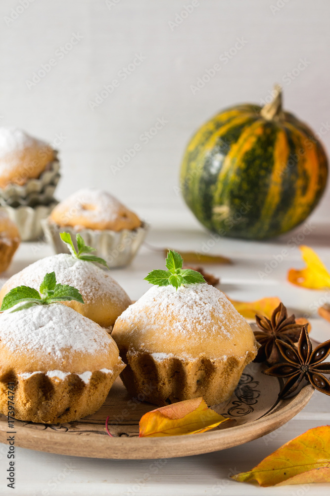 Autumn pastries. Homemade cupcakes with powdered sugar on a plate with cinnamon sticks, anise stars, pumpkins, berries of rose hip and autumn leaves 