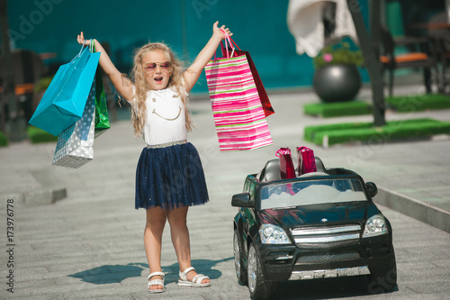 Little pretty girl driving a car. Child driving an automobile. Like a grown up. Cute girl holding shopping bags