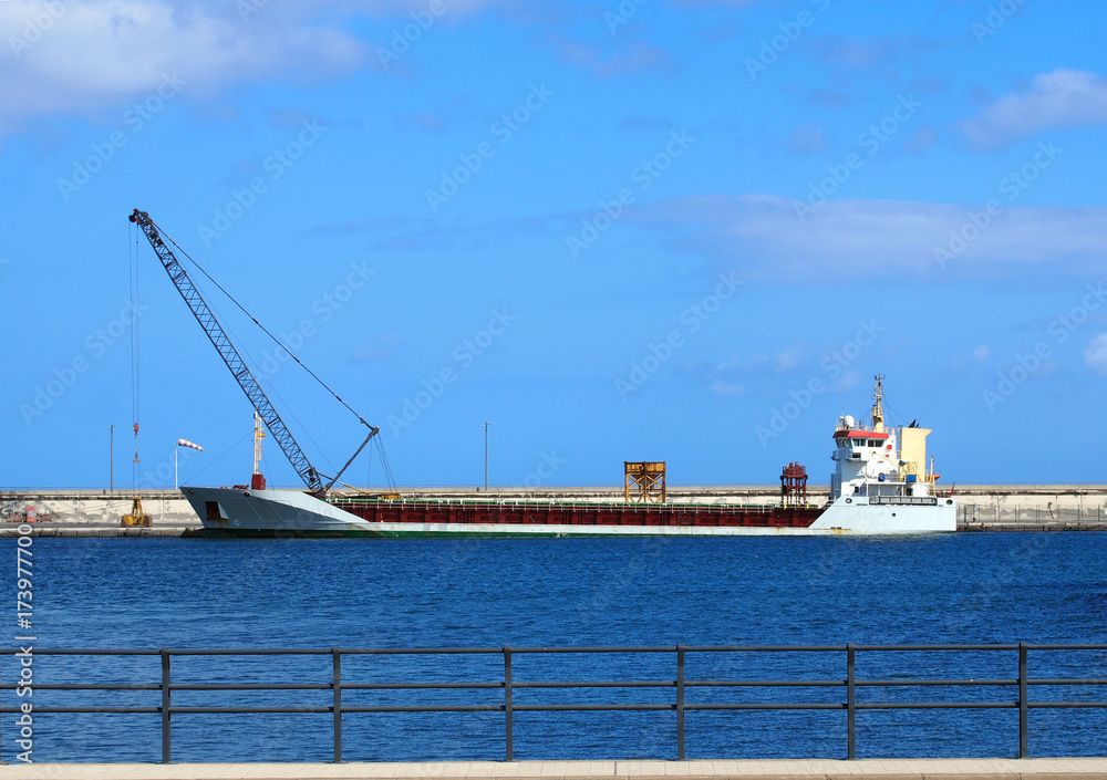 Emprty container ship in a harbour prior to loading with crane on the dock and blue sky and railings