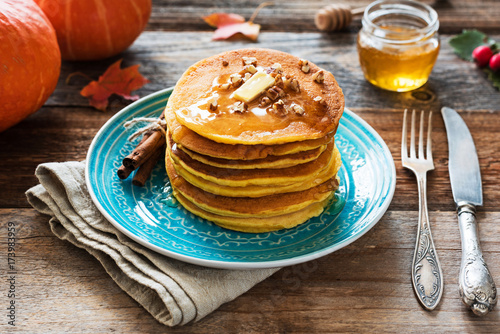 Pumpkin pancakes with pecan nuts, butter and honey on a blue plate. Seasonal autumn food