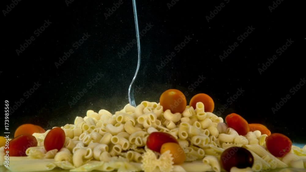 Pot with boiled salted water filled with different shapes of macaroni. Silver fork falling into water and sticked into pasta with red tomatoes. Pot with boiled salted water filled with different shapes of macaroni. Silver fork falling into water and sticked into pasta with red tomatoes.