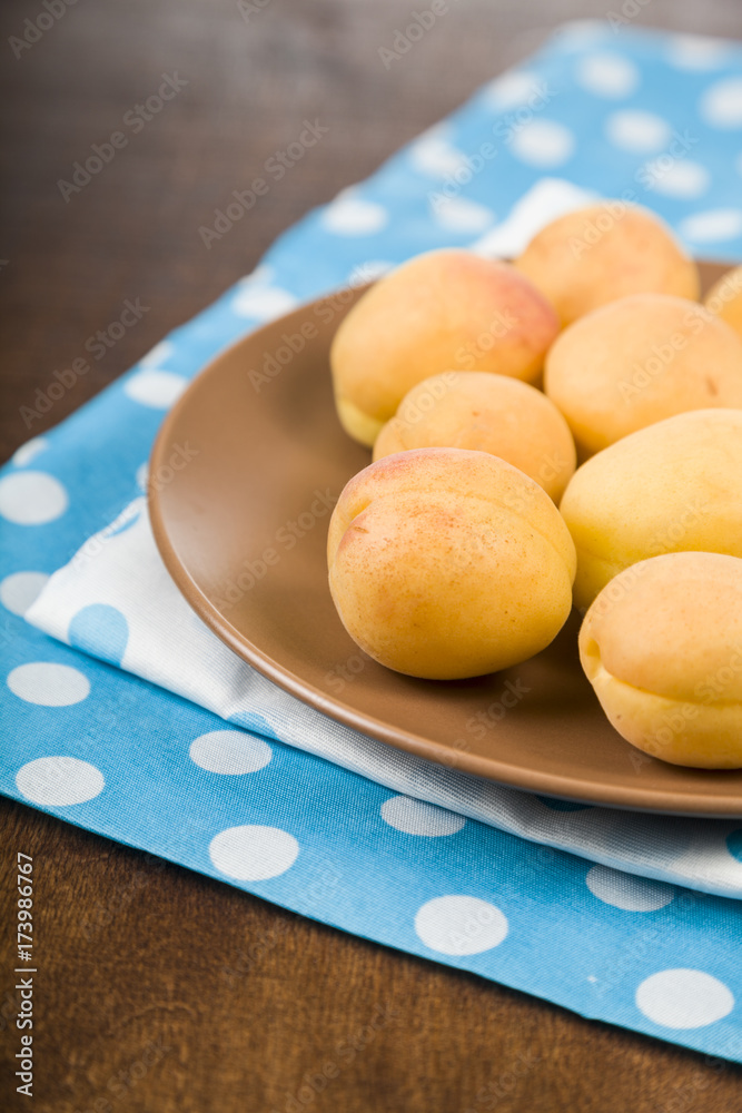 Apricots in a plate on a wooden table.