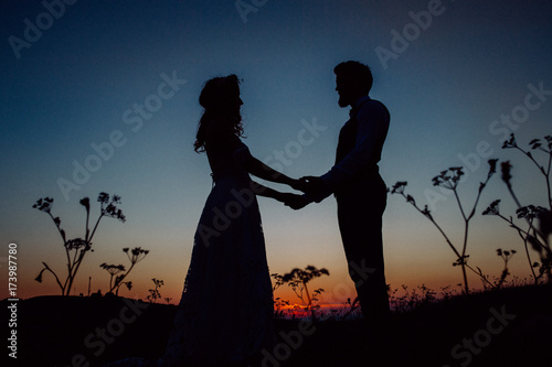 Silouethes of bride and groom on a meadow at night.