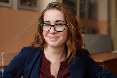 Close-up portrait of a young woman in glasses. A girl with red hair in the classroom. Business woman in training class