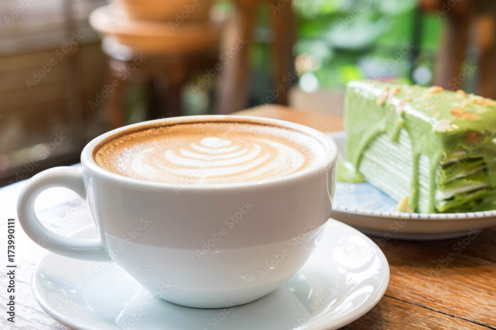 Φωτογραφία White color cup of hot coffee on plate and green tea crape cake in the backgroun