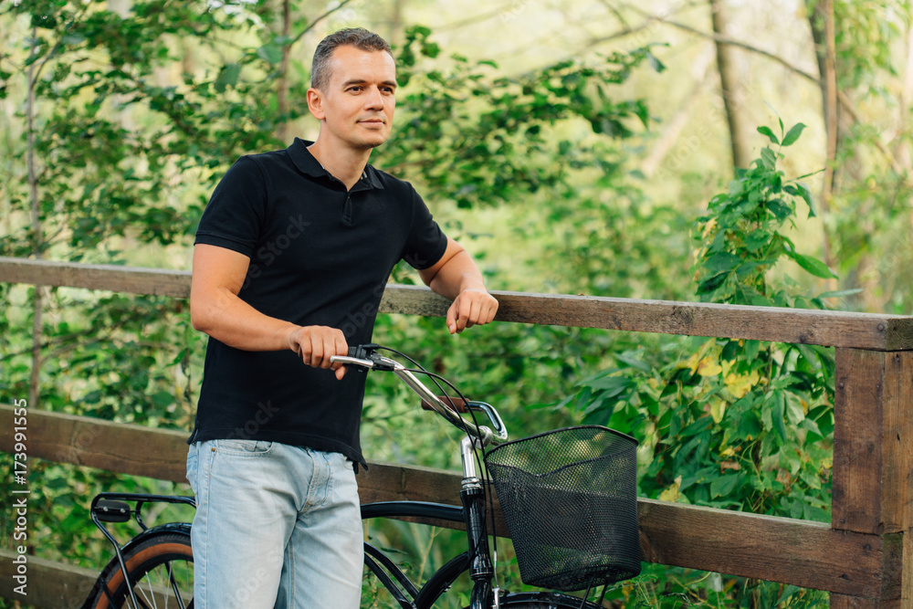 Pretty young man in casual standing with retro bicycle in park Pretty young man in casual standing with retro bicycle in park