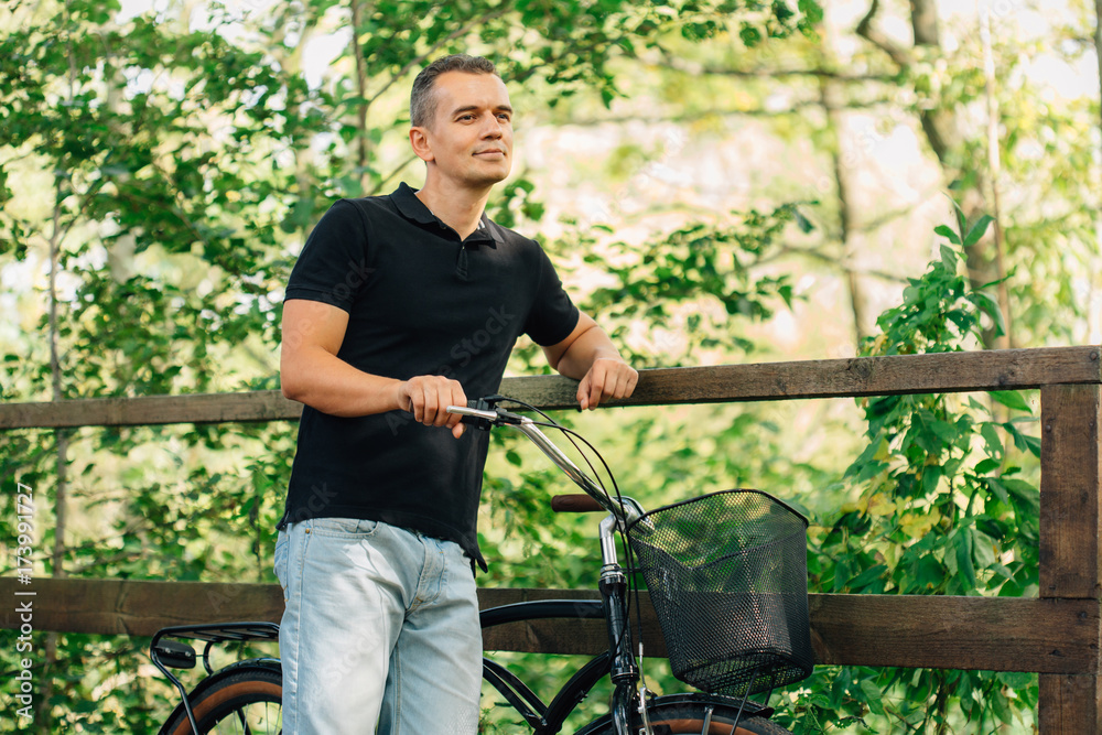 Pretty young man in casual standing with retro bicycle in park