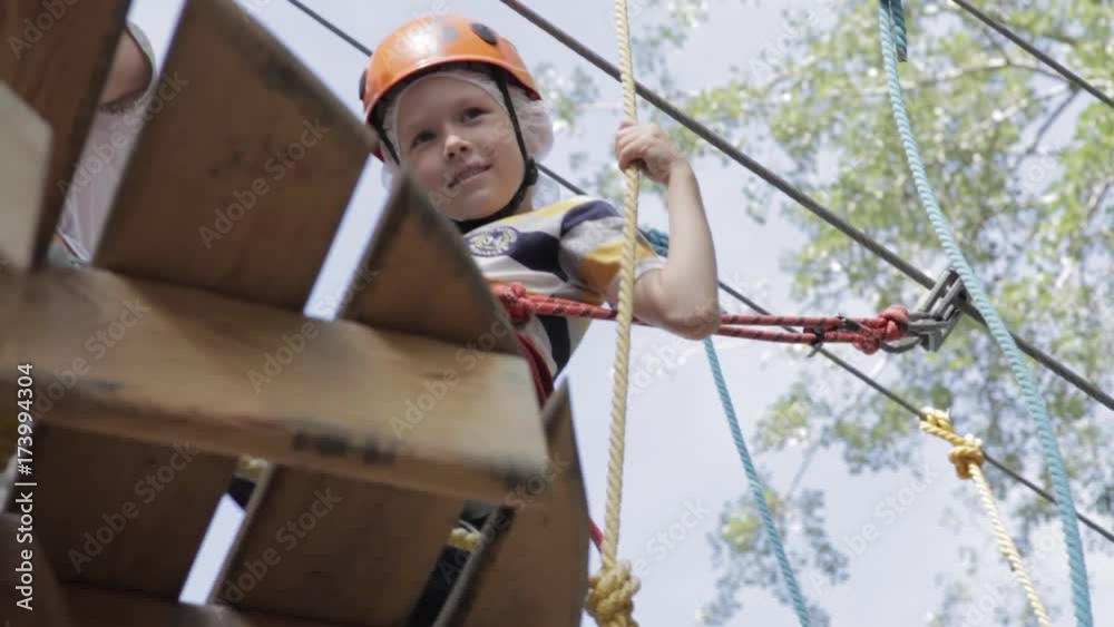 Little cute boy enjoying activity in a climbing adventure park on a summer sunny day. toddler climbing in a rope playground structure. Safe Climbing extreme sport with helmet and Carabiner. insurance Little cute boy enjoying activity in a climbing adventure park on a summer sunny day. toddler climbing in a rope playground structure. Safe Climbing extreme sport with helmet and Carabiner. insurance