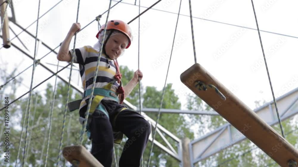 Little cute boy enjoying activity in a climbing adventure park on a summer sunny day. toddler climbing in a rope playground structure. Safe Climbing extreme sport with helmet and Carabiner. insurance Little cute boy enjoying activity in a climbing adventure park on a summer sunny day. toddler climbing in a rope playground structure. Safe Climbing extreme sport with helmet and Carabiner. insurance