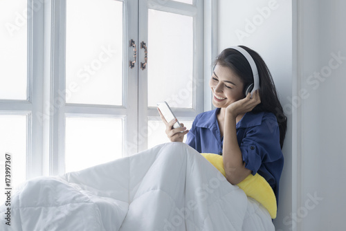 Asian women listen to music in their wireless headphones on the window with a happy smile.