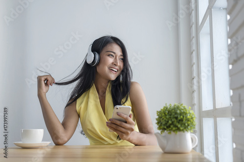 Asian women sitting to relax and listening music in wireless headphones at the cafe,holding smartphone in hand