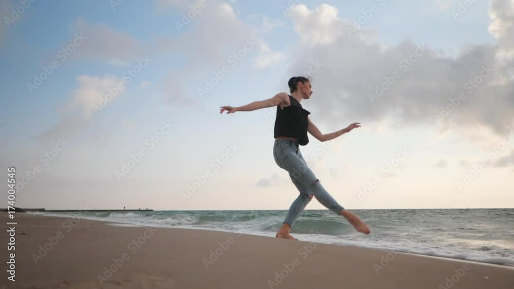 Young woman in casual style - denim and black top doing ballet at the beach. Attractive ballerina practices in jumping on sandy coastline in autumn. Slow motion. Young woman in casual style - denim and black top doing ballet at the beach. Attractive ballerina practices in jumping on sandy coastline in autumn. Slow motion.