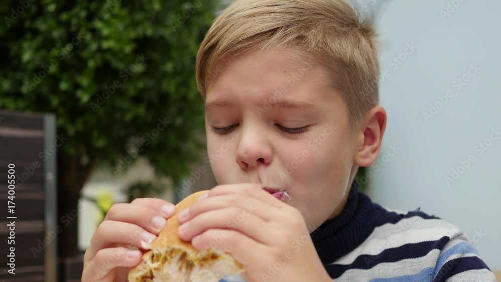 child eating a bun with chicken, cheese and greens in a fast food restaurant child eating a bun with chicken, cheese and greens in a fast food restaurant