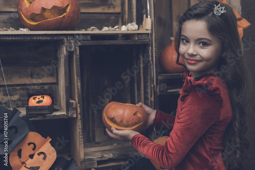 A girl in a red dress is holding a lamp from a pumpkin for Halloween