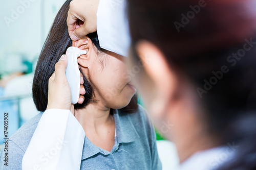 Doctor checking patient's temperature in the ear with Tympanic Thermometer, inside the clinic. Soft Focus.