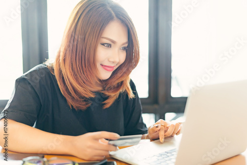 Asian stylish glasses woman designer wear black dress and red lips shopping with credit card on internet in selective focus..