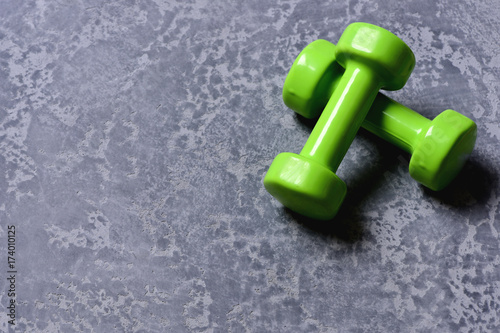 Dumbbells made of bright green plastic on grey texture background