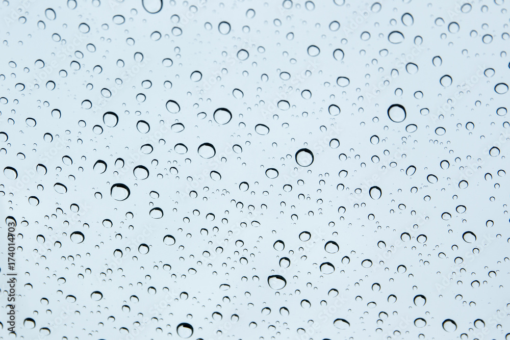 Rain drops on glass with cloudy sky background.