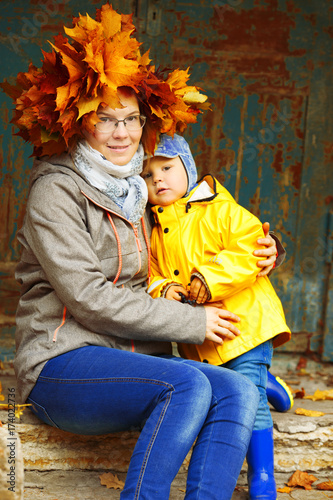 Little boy with mother on background of autumn park. Child and mom with a maple leaf. Family fall scene