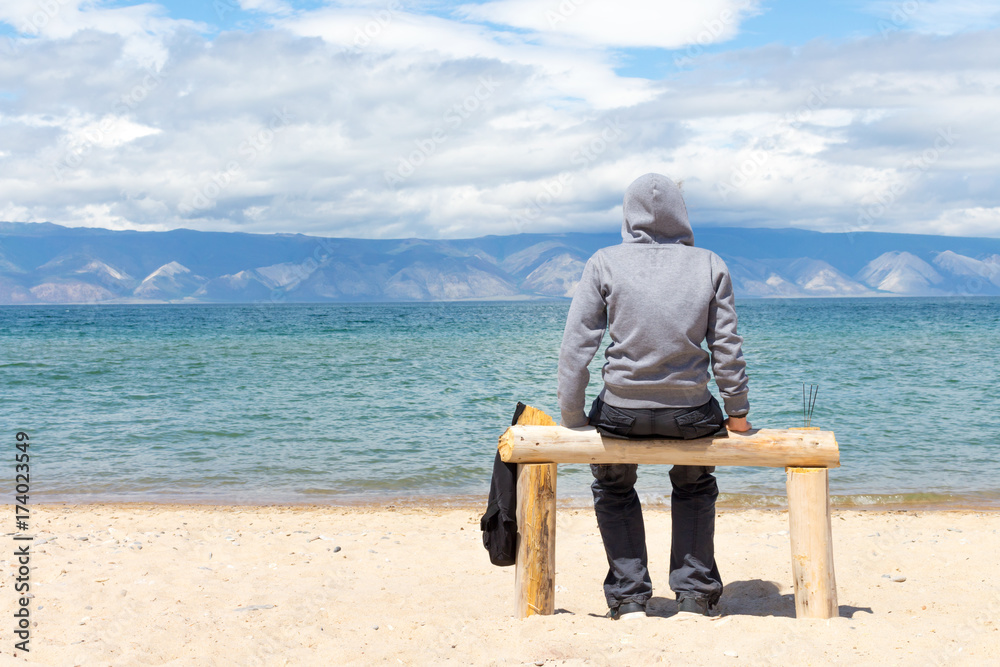 Man or woman is sitting in a hoodie on the beach. Back view