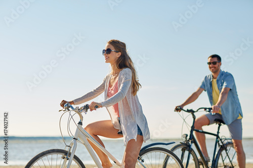 happy young couple riding bicycles at seaside