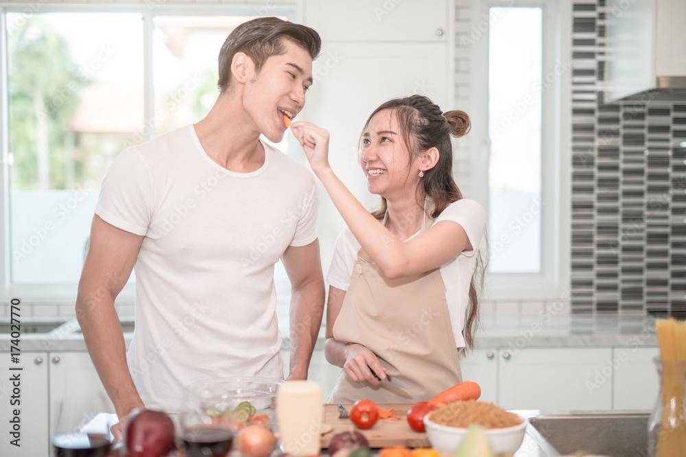 young Asian woman having her husband tasting pasta dish .happy couple in kitchen