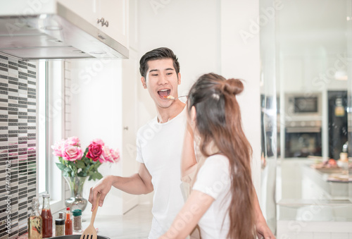 young Asian woman having her husband tasting pasta dish .happy couple in kitchen