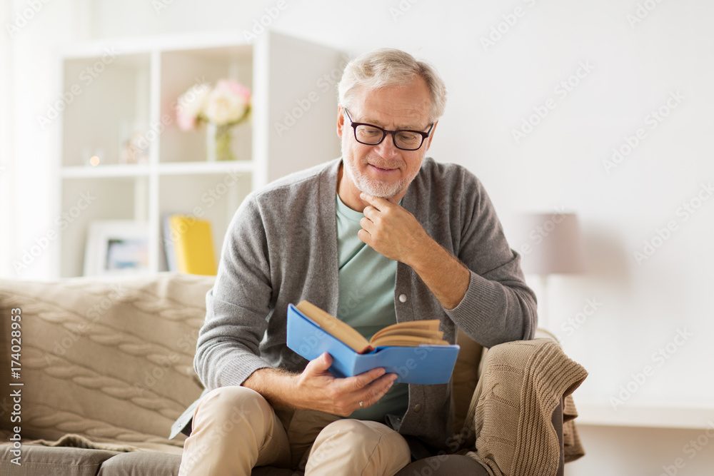 senior man on sofa reading book at home
