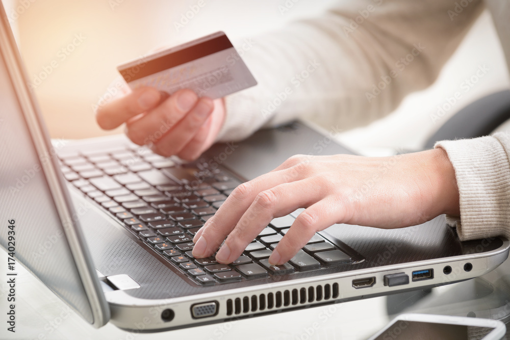 Womans hand holding credit card over laptop Womans hand holding credit card over laptop