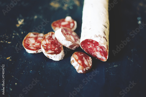 Dry cured sausage with spices on dark background photo