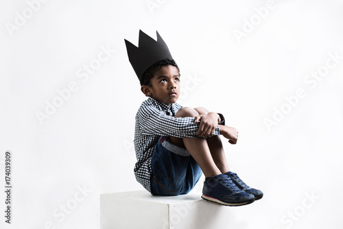 Portrait of a boy wearing a black crown sitting.