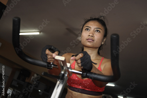 young beautiful and sweaty Asian active woman training hard cycling and riding on static bike workout at gym