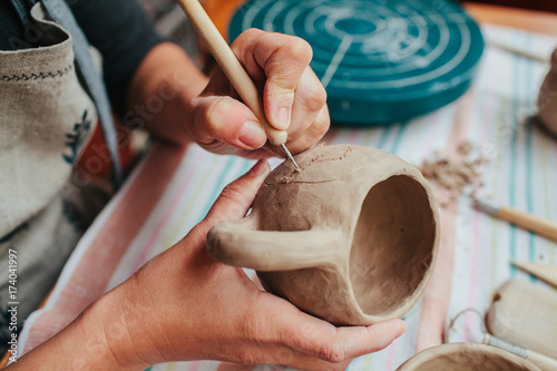 Woman potter making pattern on the ceramic cup in her workshop
