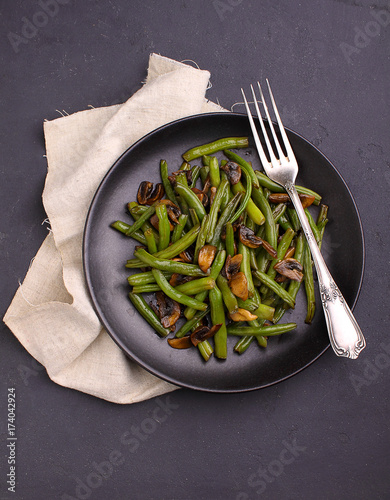 green roast beans fried with mushrooms in oriental style on a black plate on a black background