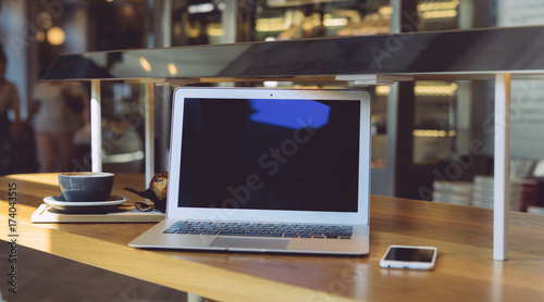 Open portable computer with blank display with copy space for your information is ready to be used for work. Modern notebook and smartphone and cup of coffee on wooden desk of a cafe. © JKstock