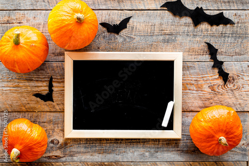 Halloween mockup. Chalkboard near paper bats and pumpkins on wooden background top view photo