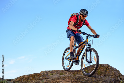 Cyclist in Red Riding the Bike Down the Rock on the Blue Sky Background. Extreme Sport and Enduro Biking Concept. © Maksym Protsenko