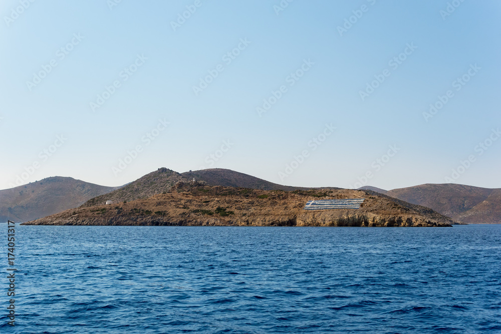 Rocky coastline with a big Greek flag in Kalymnos island, Dodecanese, Greece