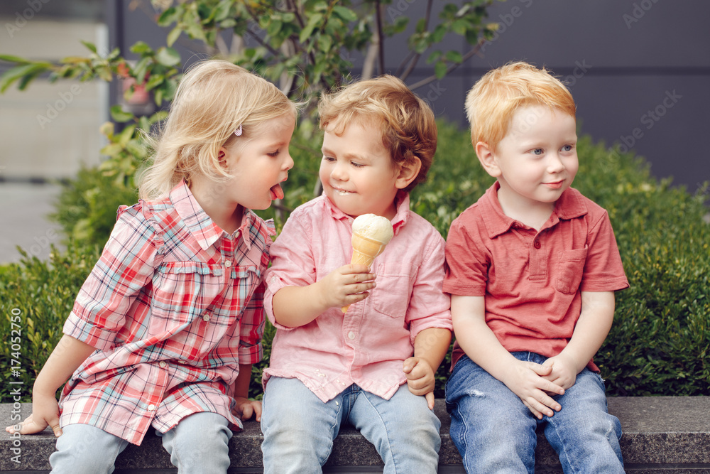 Fototapeta premium Group portrait of three white Caucasian cute adorable funny children toddlers sitting together sharing ice-cream food. Love friendship jealousy concept. Best friends forever.