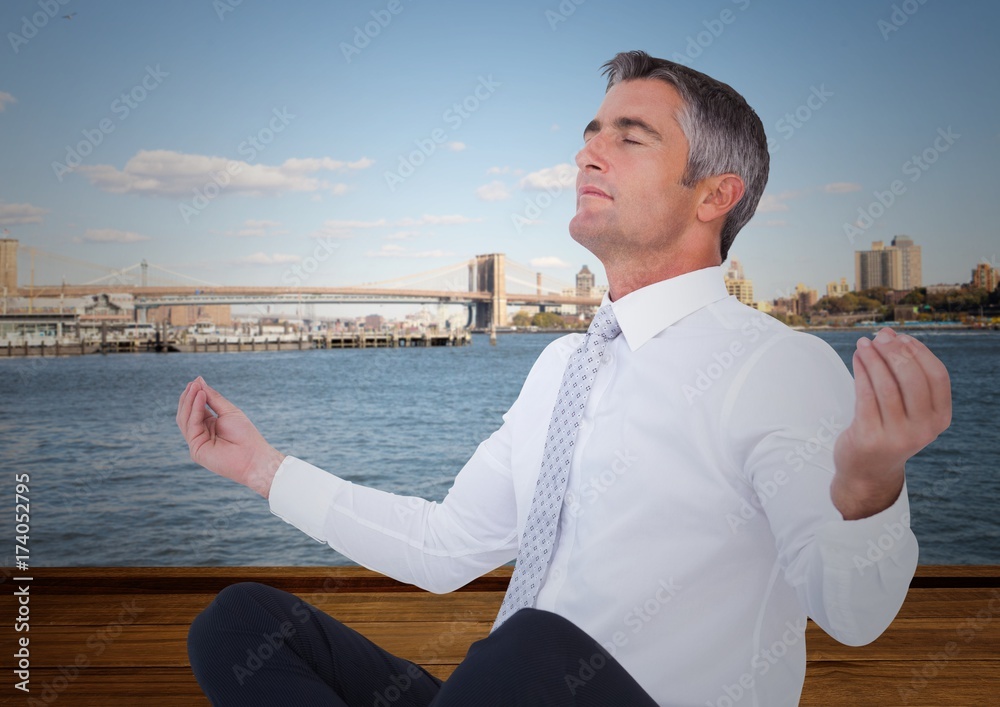 Business man meditating against water and skyline Business man meditating against water and skyline
