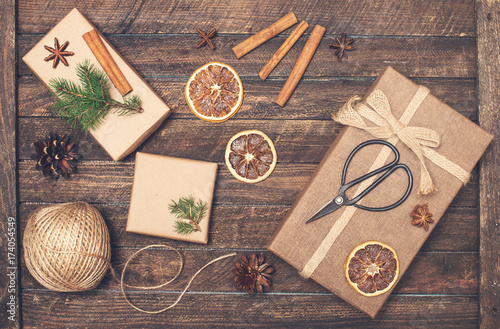 Set for Christmas gift wrapping. Presents wrapping inspirations. Gift box, ball of jute, cinnamon sticks, anise, orange slices, fer tree branches and retro scissors on rustic wooden background. 