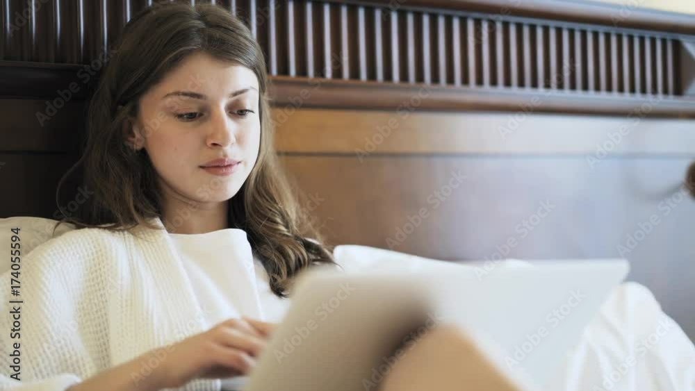 Front view of a sleepy businesswoman sitting on a hotel bed and typing at her laptop keyboard. Handheld real time close up shot Front view of a sleepy businesswoman sitting on a hotel bed and typing at her laptop keyboard. Handheld real time close up shot
