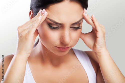 pain. Portrait of a beautiful young brunette with bare shoulders, severe headaches, migraine, colds. The concept of treatment. Holds his hand to his forehead.
