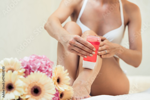 Fit young woman waxing her legs with a portable roll-on depilatory wax heater for painless hair removal at home photo